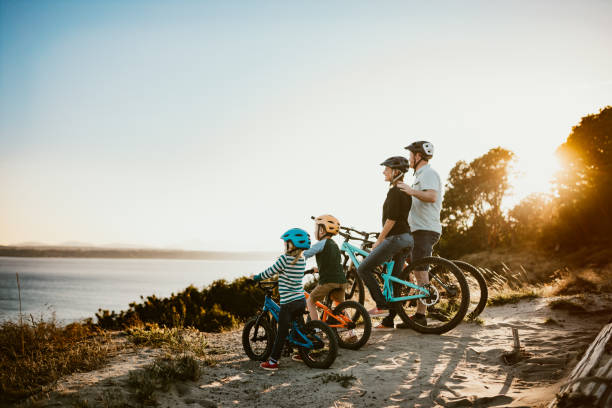 Family Mountain Bike Riding Together on Sunny Day A father and mother ride mountain bikes together with their two small children.  A fun way to spend time together and exercise while on vacation in the Seattle, Washington area.  They stop and look at a view of the Puget Sound from a ridge top. puget sound photos stock pictures, royalty-free photos & images