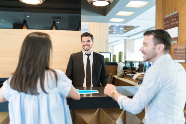 istock Clerk Smiling And Looking At Couple In Lobby 1164434157