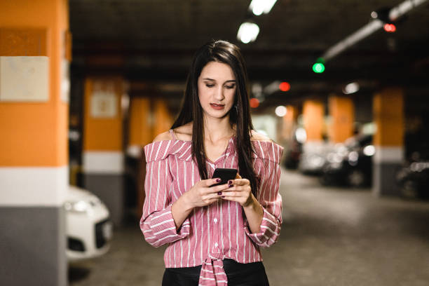 istock Young woman using smart phone at car parking 1164435002