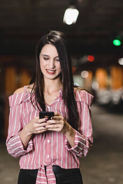 istock Young woman using smart phone at car parking 1164435004