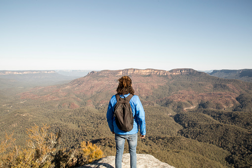 One young latin man, wearing an electric blue winter jacket and blue jeans, contemplating the Blue Mountains in Australia