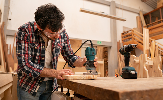 Carpenter making a piece of furniture and using a router at his wood workshop