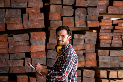Portrait of a man working at a wood factory doing the inventory on the logs and looking at the camera smiling