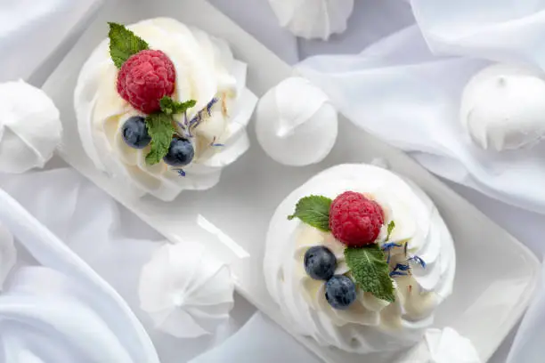 Photo of Dessert Pavlova with raspberries, blueberries and mint on a white fabric.