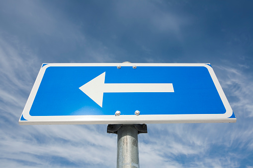 traffic sign arrow pointing left against sky