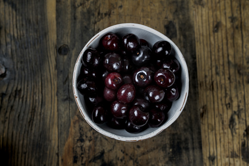 horizontal view of fresh organic ripe black cherries in a white bowl on a rustic wooden table
