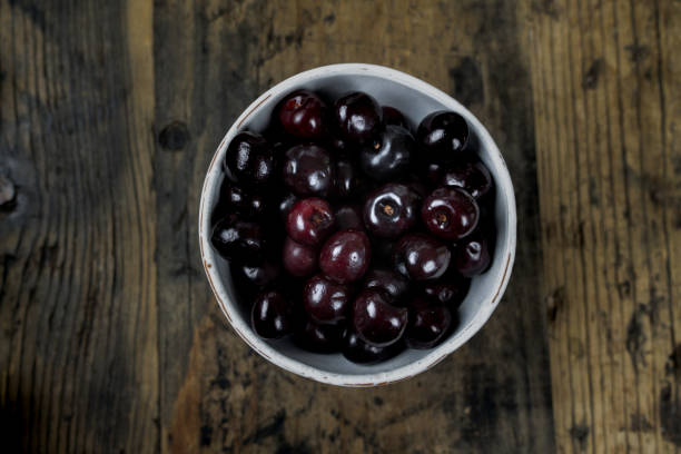 świeże organiczne dojrzałe czarne wiśnie w białej misce na rustykalnym drewnianym stole - black cherries zdjęcia i obrazy z banku zdjęć
