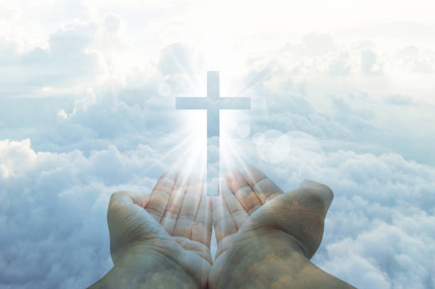 istock hands cupped with a shining white cross hovering above on a sunny blue daytime sky with fluffy clouds 1164501448