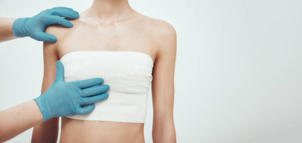 Increase your breast size. Cropped photo of woman waiting for plastic surgery while surgeons in blue medical gloves measuring her breast stock photo