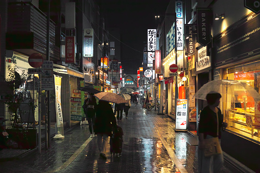 Tokyo, Japan - 11/6/2018: People walking down a wet street in Koenji at night