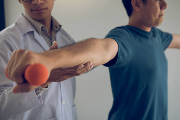 istock Asian physiotherapist helping a patient lifting dumbbells work through his recovery with weights in clinic room. 1164509168