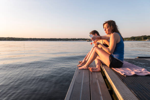 istock young women sit on a jetty at lake, using sun lotion 1164509244