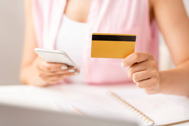 istock Hand of female shopper with plastic card using smartphone to make online order 1164510514