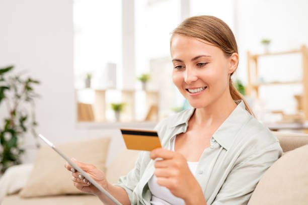 istock Young woman with tablet reading data on card while paying for online order 1164510549