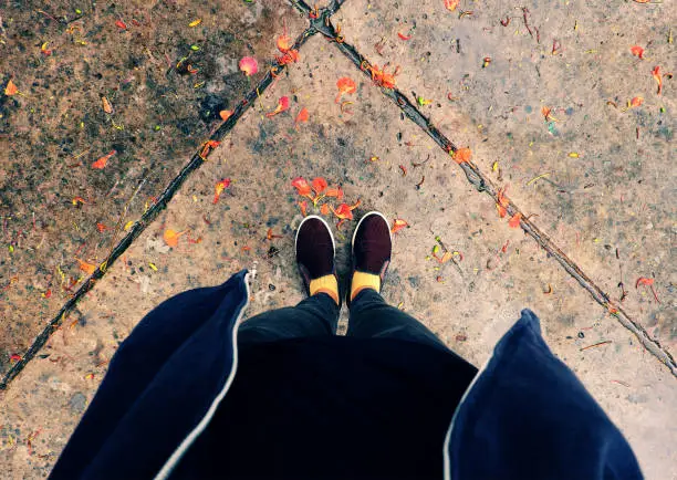 Top view of woman feet in black clothes stand outdoor yard with orange petals fall in raining day