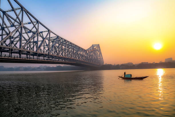 Historic Howrah bridge with boat on river Ganges at Kolkata, India Howrah bridge Kolkata on river Ganges at sunrise with winter haze and a wooden boat seen travelling through the Ganges. Howrah bridge is one of the busiest cantilever bridge in India cantilever bridge stock pictures, royalty-free photos & images