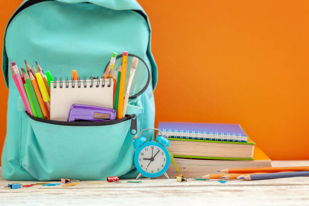 istock School Backpack with different supplies and alarm clock on orange background. Concept back to school 1164520772