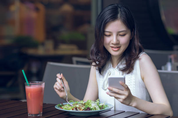 istock Beautiful Asian young woman having healthy breakfast in modern restaurant and using mobile phone 1164521097