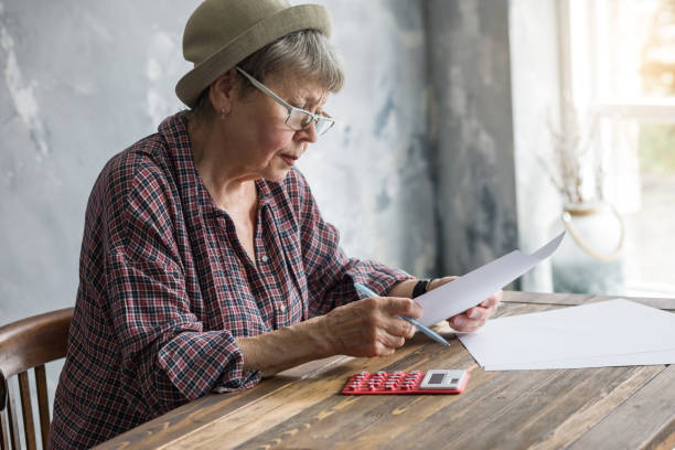 An elderly woman with financial documents and a calculator. stock photo