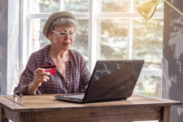 An elderly woman with a laptop and a credit card. stock photo