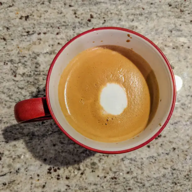 A hot flatwhite coffee on a granite countertop Inna red cup