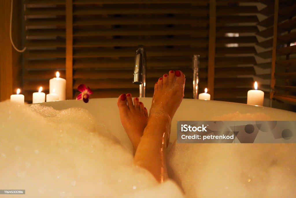 Feet of the young woman in bath with foam and candles Back view of the feet of the young woman in bath with foam and candles Bathtub Stock Photo