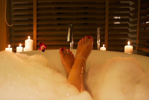 Feet of the young woman in bath with foam and candles Back view of the feet of the young woman in bath with foam and candles indulgence photos stock pictures, royalty-free photos & images