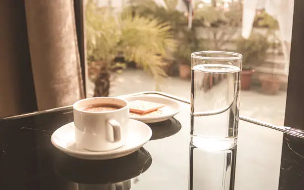 White Coffee cup placed on the dining table while morning sunlight coming from the window. Tasty cup of sweet smelling morning coffee, Vintage style color effect. Happy weekend concept.