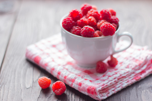 white Cup filled with fresh ripe raspberry on wooden background