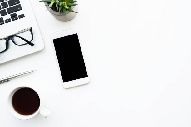 istock White smartphone with blank mock up screen is on top white office desk table with laptop computer, cup of coffee and supplies. Top view with copy space, flat lay. 1164539655
