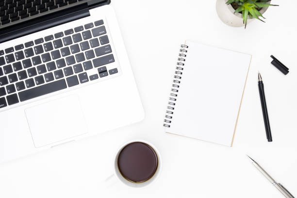 istock Blank small notebook page is on top of white office desk table with pen, laptop computer and supplies. Top view, flat lay. 1164539668