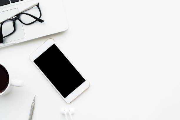 istock White smartphone with blank mock up screen is on top white office desk table with laptop computer, cup of coffee and supplies. Top view with copy space, flat lay. 1164539672