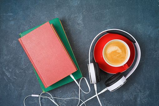 Audio book concept with old book, headphones and coffee cup over blackboard background. Top view from above