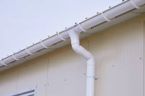 White plastic rain guttering system. Guttering drainage pipe exterior. Background of sandwich panel
