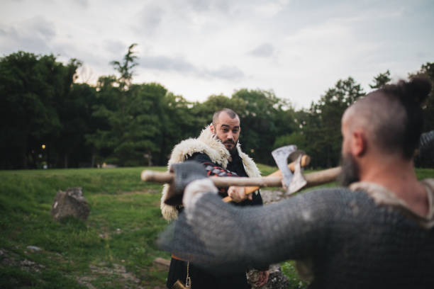 Medieval warriors in chain mail and a robe, with axes fighting outdoors.