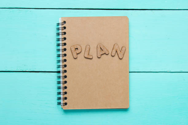 istock I have an plan! Notebook with craft paper with word PLAN on blue wooden table. 1164558073