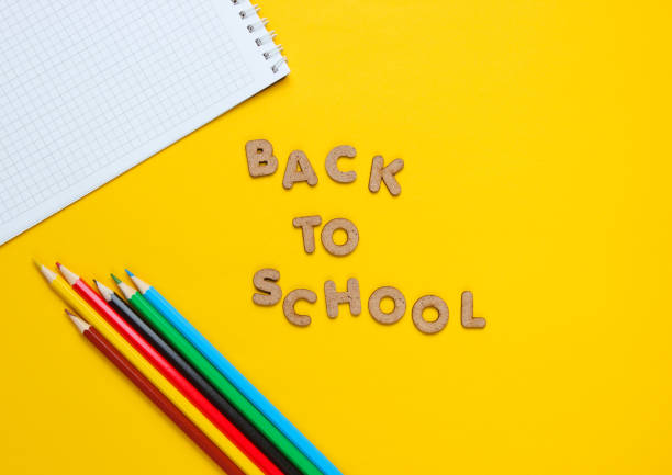 istock School time concept. Multicolored pencils, notebook on yellow background and words back to school with wooden letters 1164558122