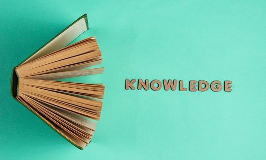 Open old book on blue background with the word knowledge of wooden letters. Top view, minimalism