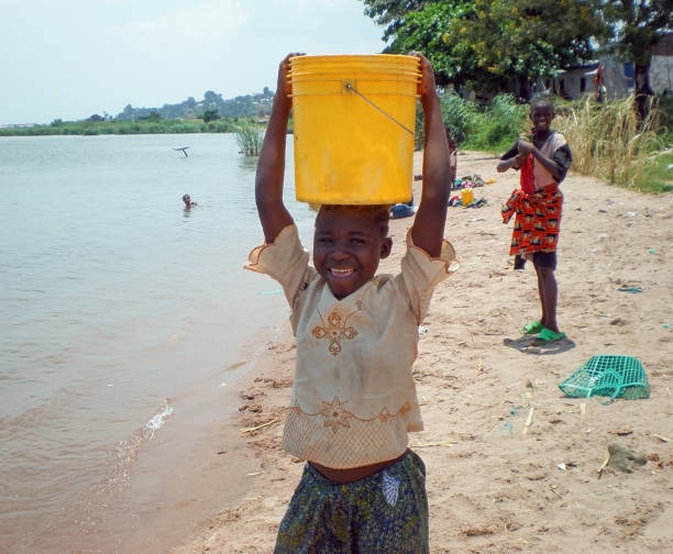 Girl on the coast of Lake Tanganyika carries a bucket of water on his head, it happens to 28.01.2010. in DRC Congo Africa stock photo