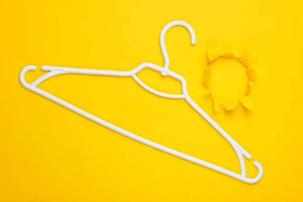 istock White plastic hanger on yellow background with torn hole. Minimalism shopping concept. Top view 1164559990