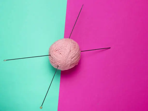 Home hobbies concept. Wool balls of thread with knitting needles on colored background. Top view