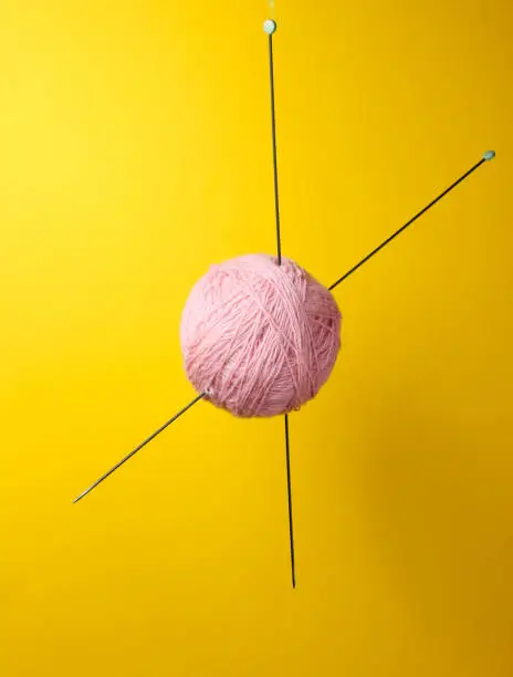 Home hobbies concept. Wool balls of thread with knitting needles on yellow background.