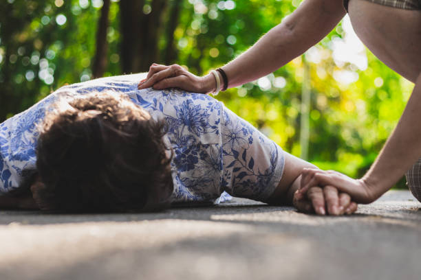 Old woman lying on the ground helped by teenager stock photo