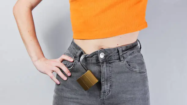 The concept of chastity. The lock hangs on women's jeans on a gray background. Crop photo, studio shot