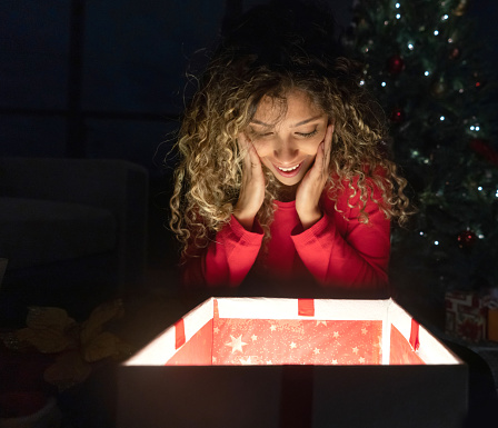 Portrait of a happy woman opening a Christmas gift and looking surprised â holidays concepts