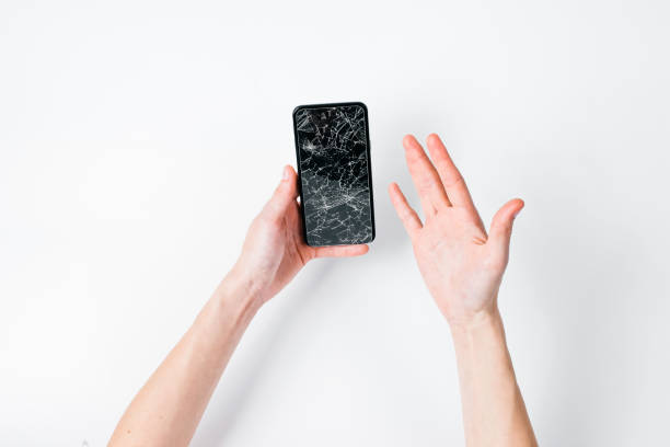 istock Female hands hold a smartphone with a broken screen through torn hole of white background 1164563098