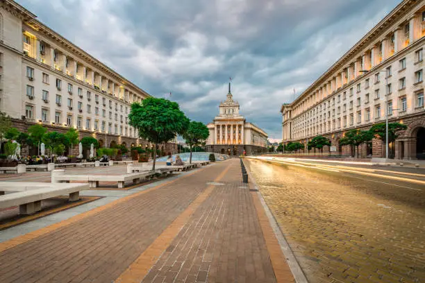 Panoramic long exposure photo from Sofia city centre in Bulgaria, Eastern Europe during twilight / rush hour with all the surrounding buildings night illumination. Including the iconic architecture of: the old house of parliament, ministry and presidency. Dragged shutter technique used to capture the blurred headlight/taillights from the road traffic. Shot on Canon full frame EOS R system for premium quality.
