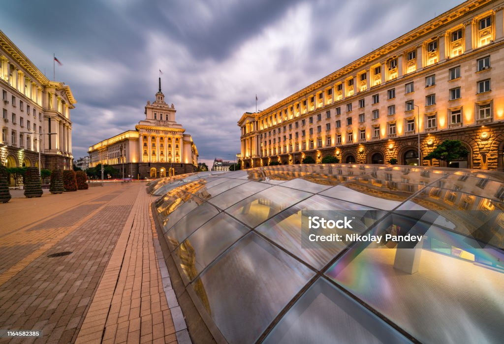 Long exposure, panoramic view of downtown Sofia city in Bulgaria, Eastern Europe - creative stock image Panoramic long exposure photo from Sofia city centre in Bulgaria, Eastern Europe during twilight / rush hour with all the surrounding buildings night illumination. Including the iconic architecture of: the old house of parliament, ministry and presidency. Dragged shutter technique used to capture the blurred headlight/taillights from the road traffic. Shot on Canon full frame EOS R system for premium quality. Sofia Stock Photo