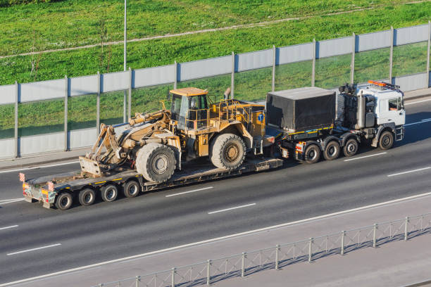 istock Truck with a long trailer platform for transporting heavy machinery, loaded big tractor with bucket. Highway transportation. 1164584323