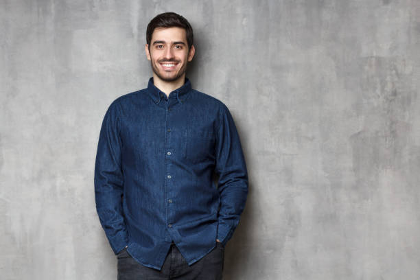 istock Young man smiling, dressed in blue denim shirt, standing isolated on gray wall background with copy space 1164586370